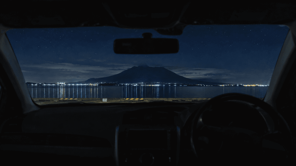 夜のマリンポートかごしまの駐車場から車越しに見る錦江湾と桜島のシルエット